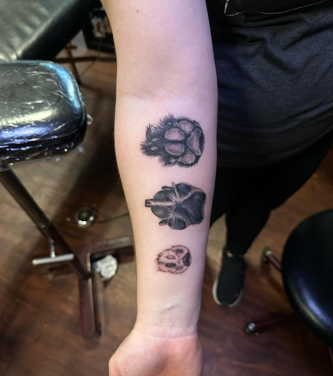 Forearm with three small black flower tattoos in a row, indoors on a tattoo chair