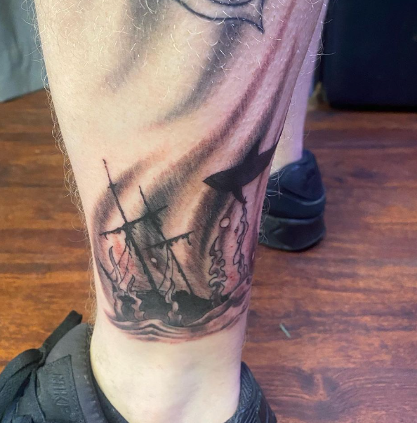Tattoo on lower leg showing a shipwreck scene with dark ink and red highlights