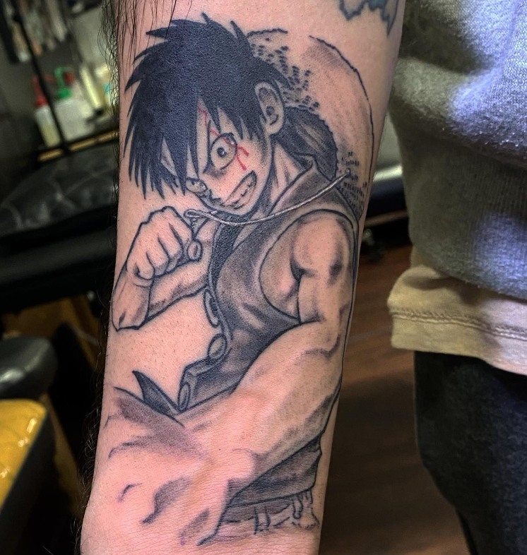 Anime-style tattoo of a fierce black-haired fighter with a clenched fist on a person’s forearm.