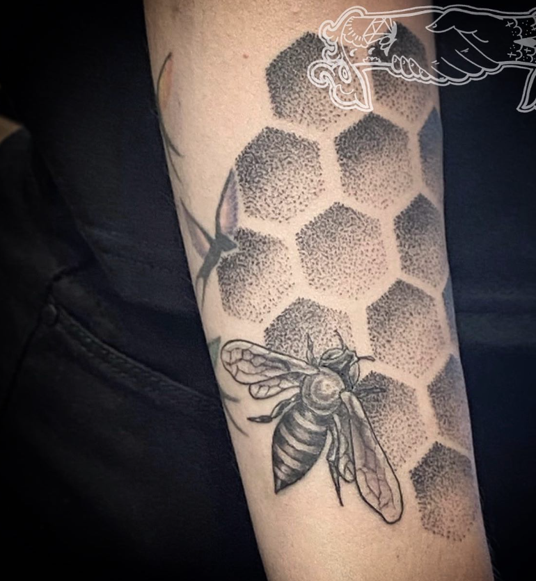 Close-up of a black-and-gray bee tattoo over hexagonal honeycomb on skin