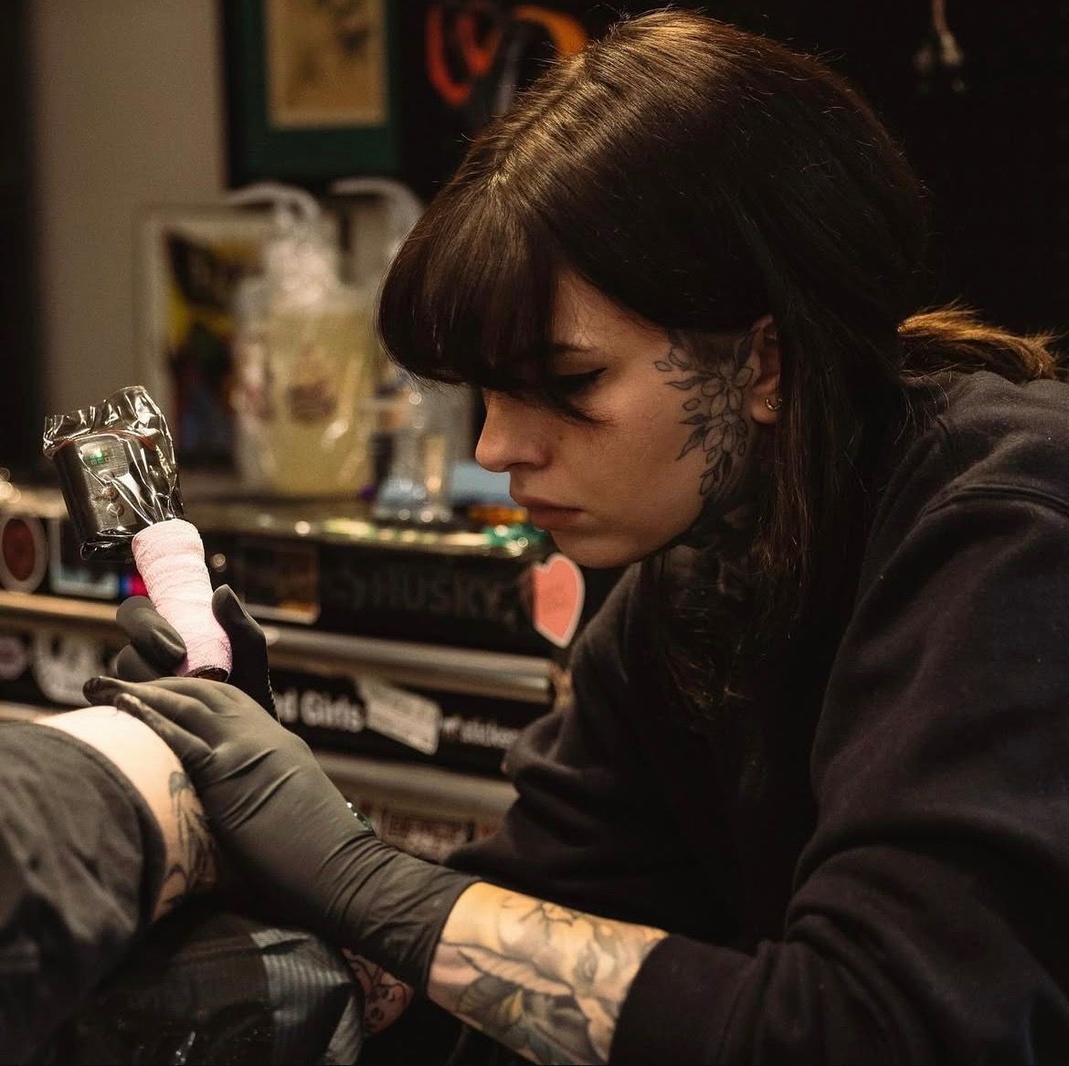 Tattoo artist working on a client’s arm in a dim studio, focused on inking with a tattoo machine