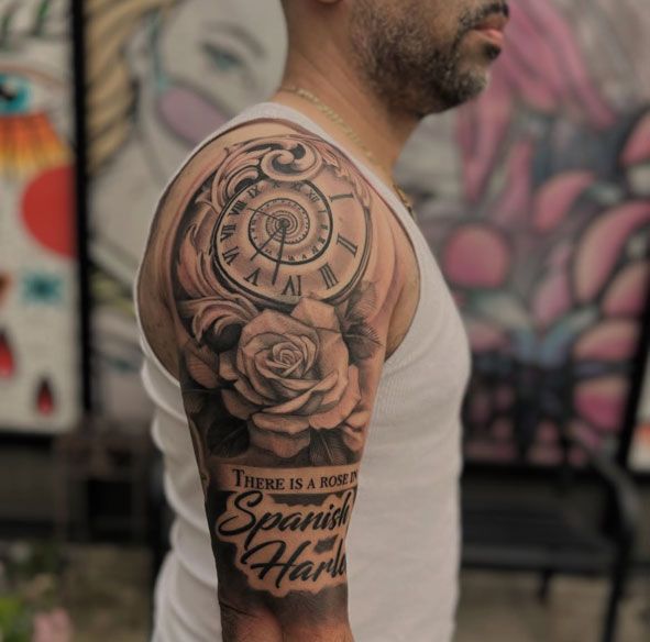 Side view of a man showing a black-and-gray tattoo sleeve with a clock, roses, and script text on his upper arm