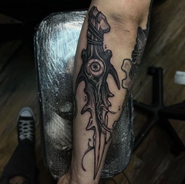 Close-up of a leg tattoo featuring a dark abstract dagger-like design on a seated person's calf