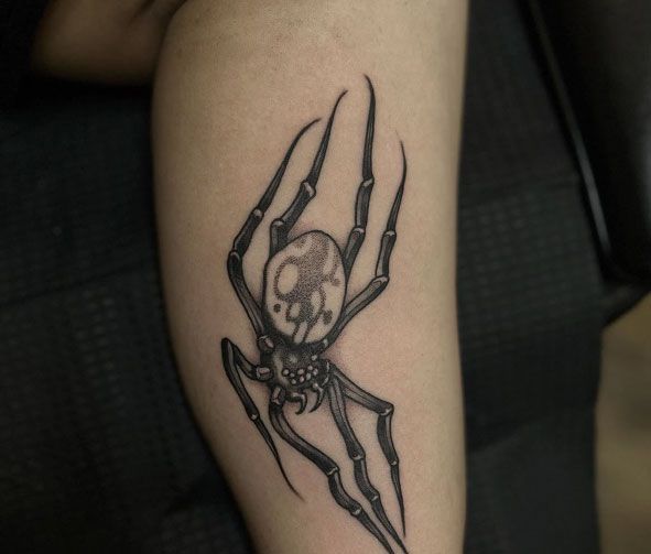 Black spider tattoo on a person’s forearm, with a skull-like body detail.