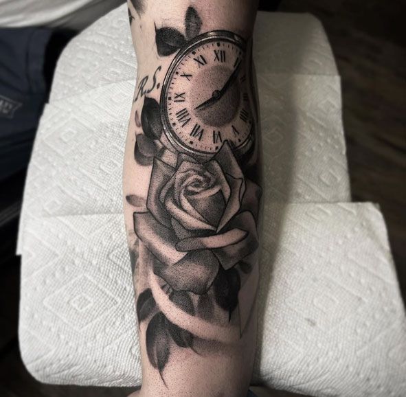 Forearm tattoo with a rose, clock, and butterfly in black and gray shading