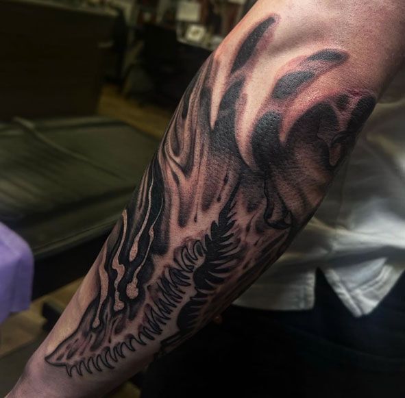 Close-up of a forearm with a black tribal-style tattoo, showing a winged design on the skin