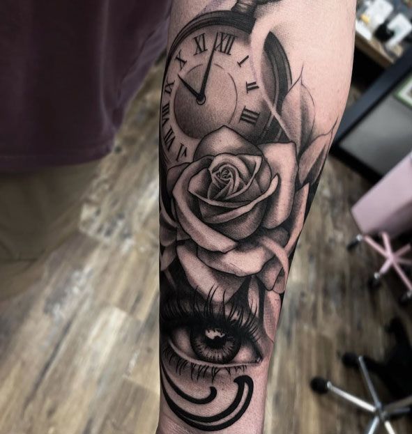 Black-and-gray forearm tattoo with a clock, rose, eye, and crescent moon design