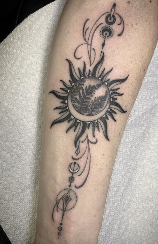 Black sun tattoo with ornamental circles and dots running vertically along a forearm.