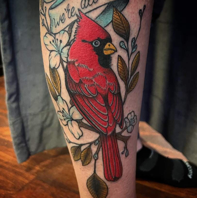 Tattooed leg with a bright red cardinal and floral designs