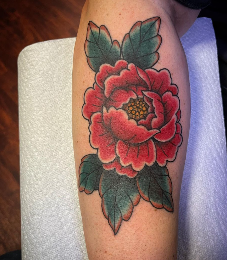 Red floral tattoo with green leaves on a forearm