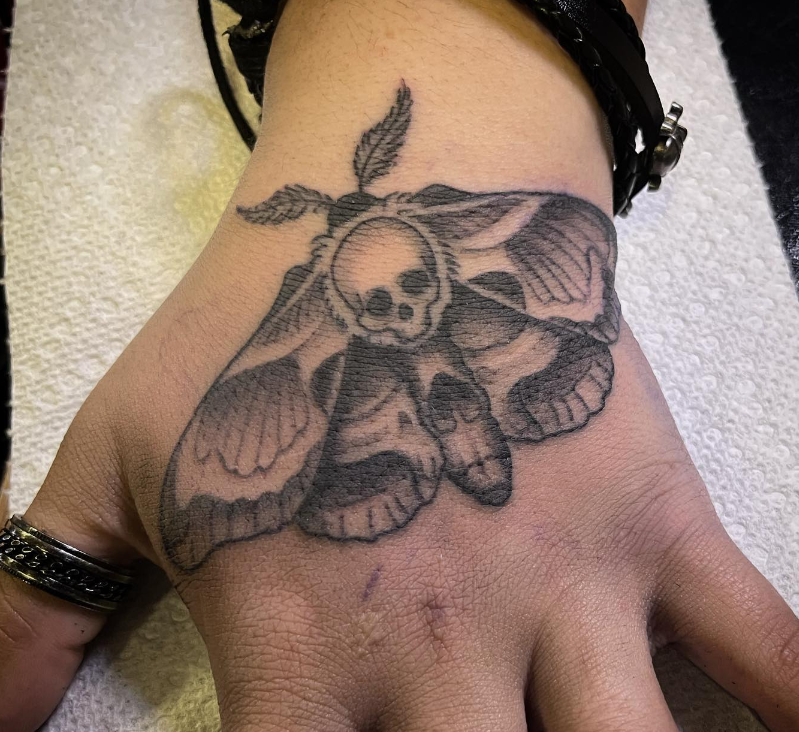 Black-and-gray skull and moth tattoo on the back of a hand