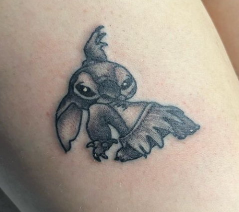 Small black-and-gray tattoo of a stylized creature with large ears and a leaf-like tail on skin
