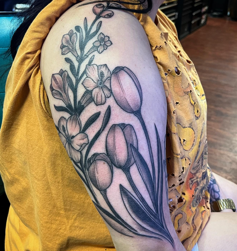 Floral tattoo on a person’s upper arm in black and gray linework with purple shading