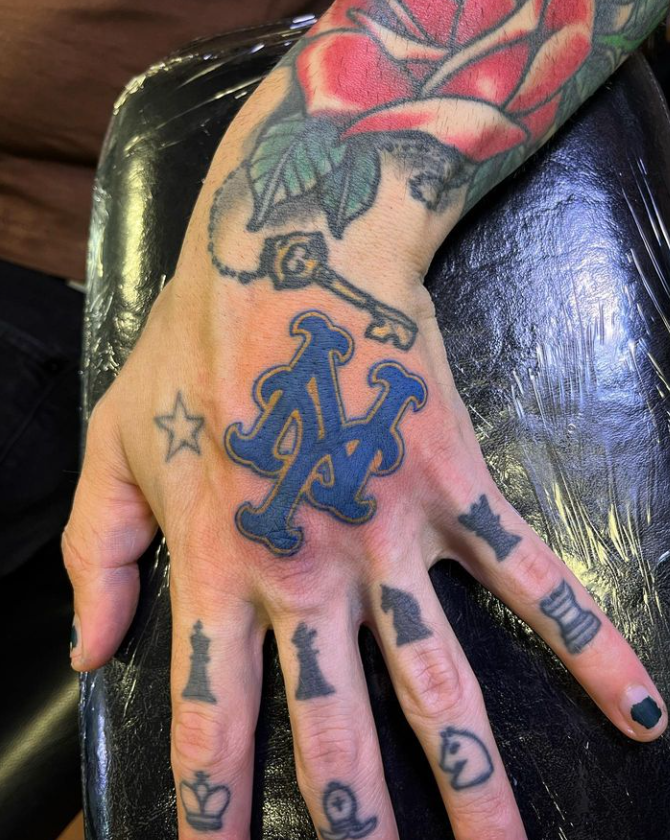 Tattooed hand with black-painted nails showing a blue NY logo tattoo on the back of the hand