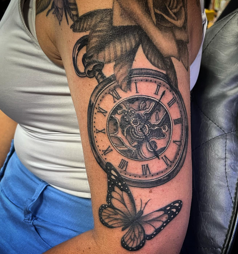 Forearm tattoo with a vintage clock and butterfly, in black ink on skin