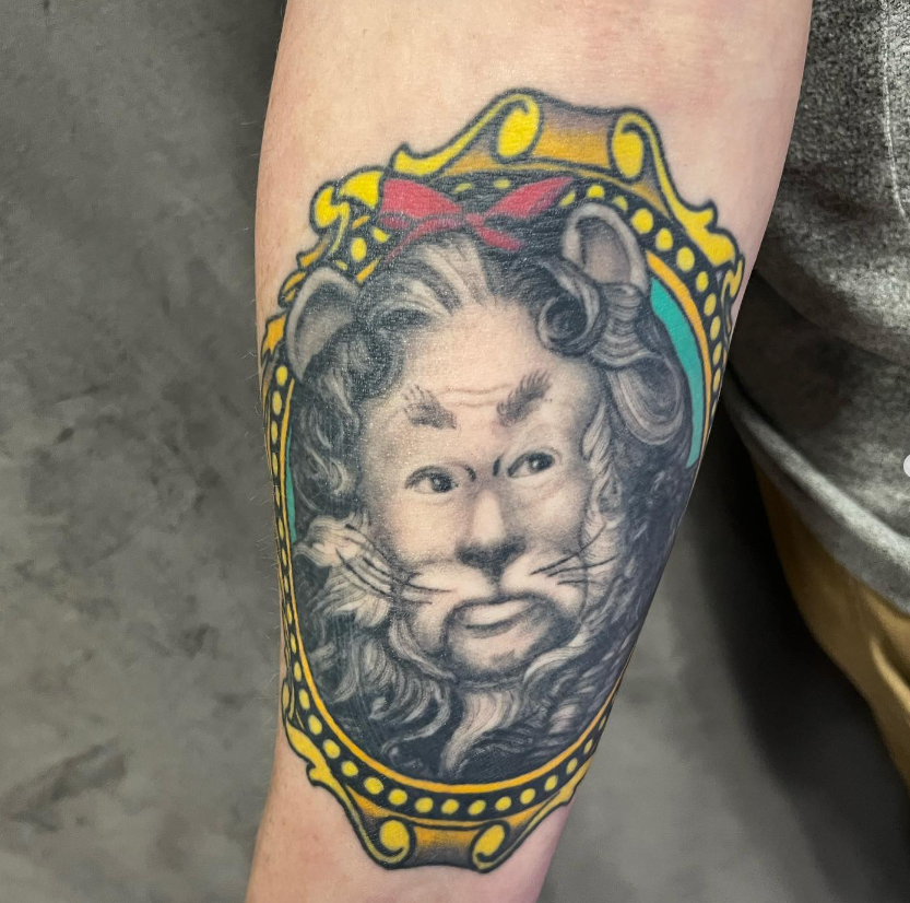 Black-and-gray lion tattoo with a yellow crown on a forearm