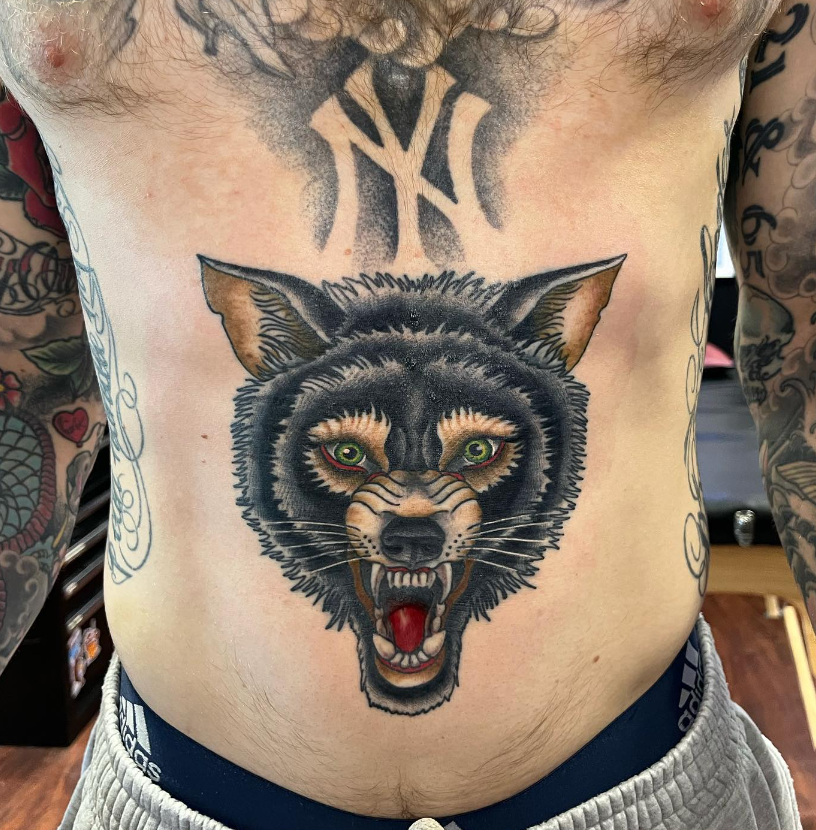 Torso with large black wolf-head tattoo centered on the abdomen, mouth open and teeth bared.