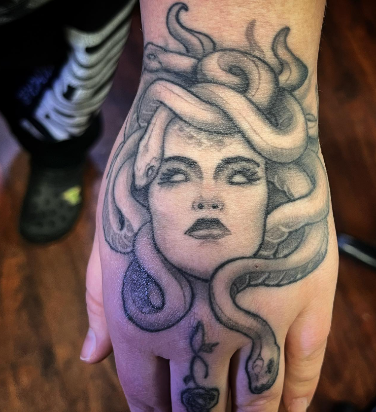 Medusa-style tattoo on the top of a hand, with flowing snakes and a shaded face