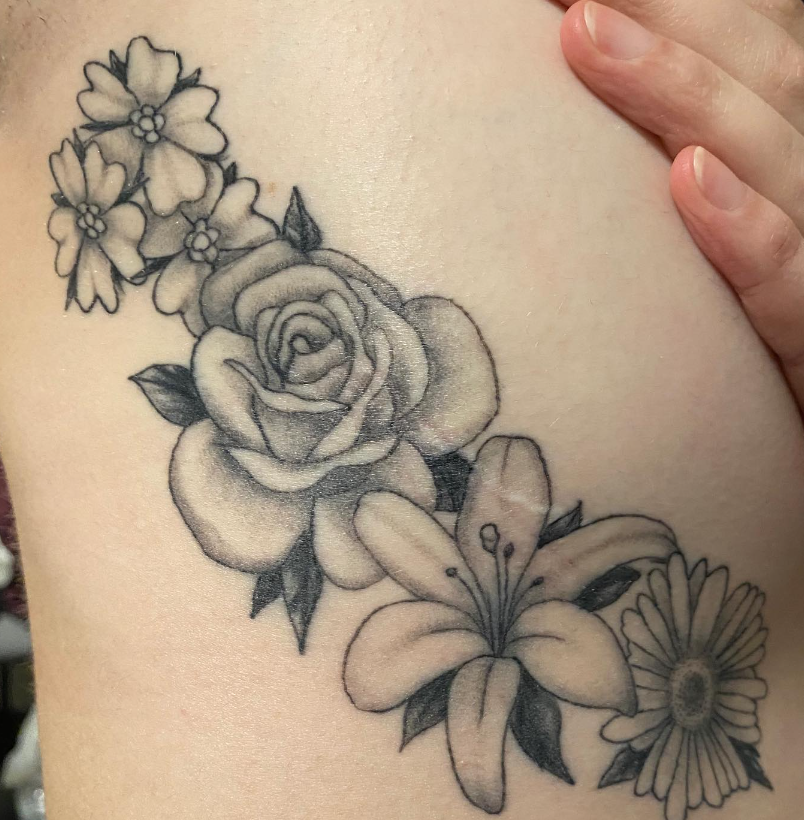 Black-and-gray floral tattoo on skin, with roses, daisies, and leaves.
