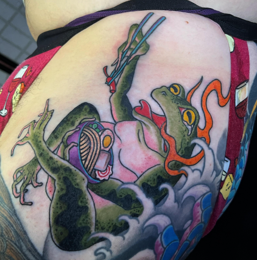 Colorful tattoo of cartoon frogs and red coral on skin, with a central frog head and green limbs