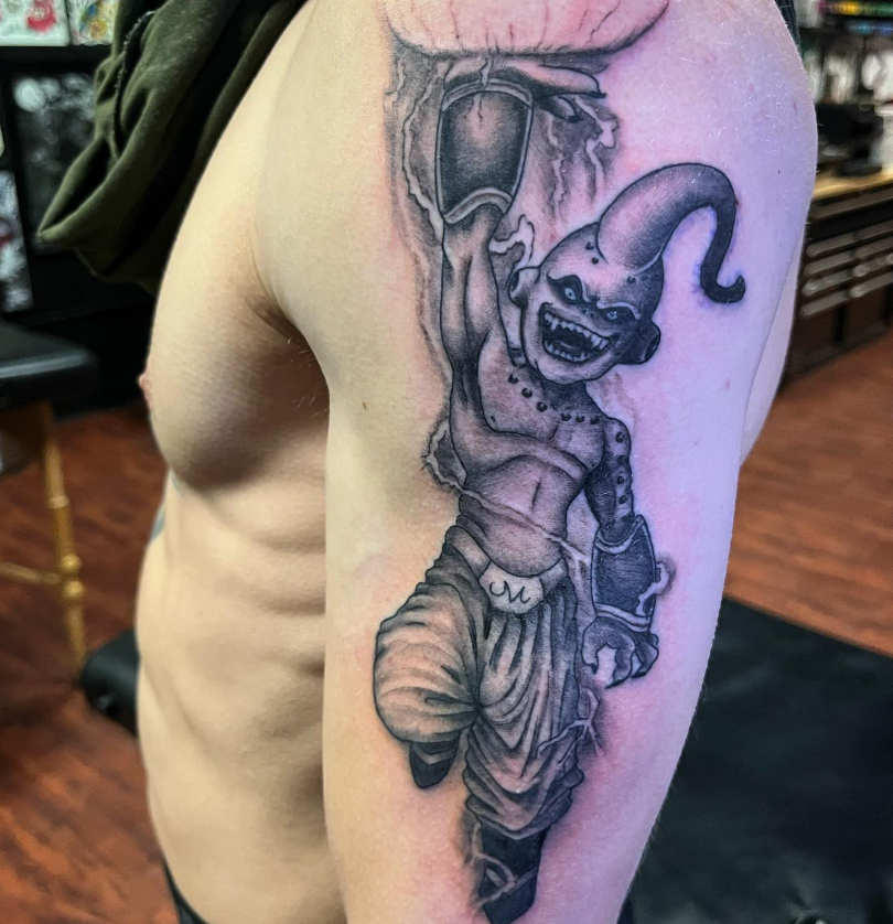 Black-and-gray tattoo of a grinning jester on a person’s upper arm