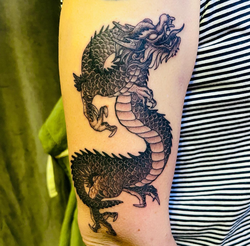 Dragon tattoo on a person’s upper arm beside a striped shirt
