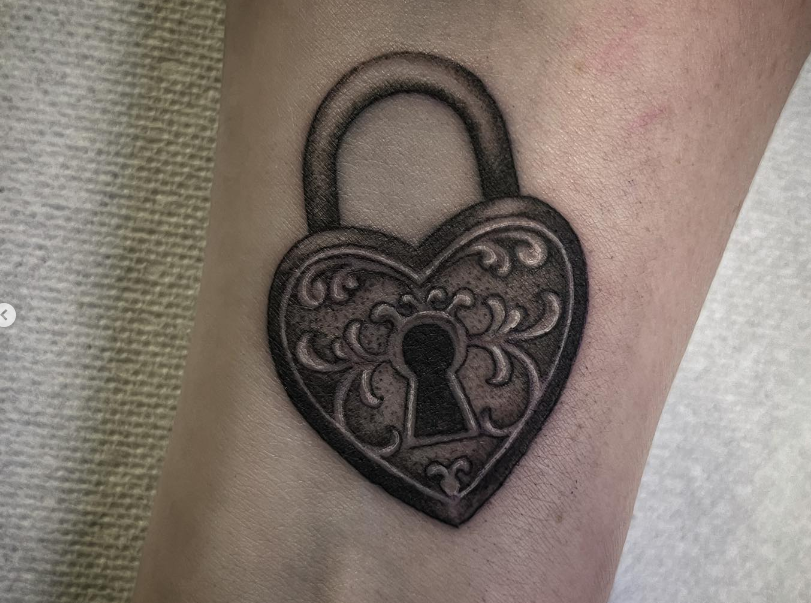 Black heart-shaped padlock tattoo on skin with ornamental details and keyhole.