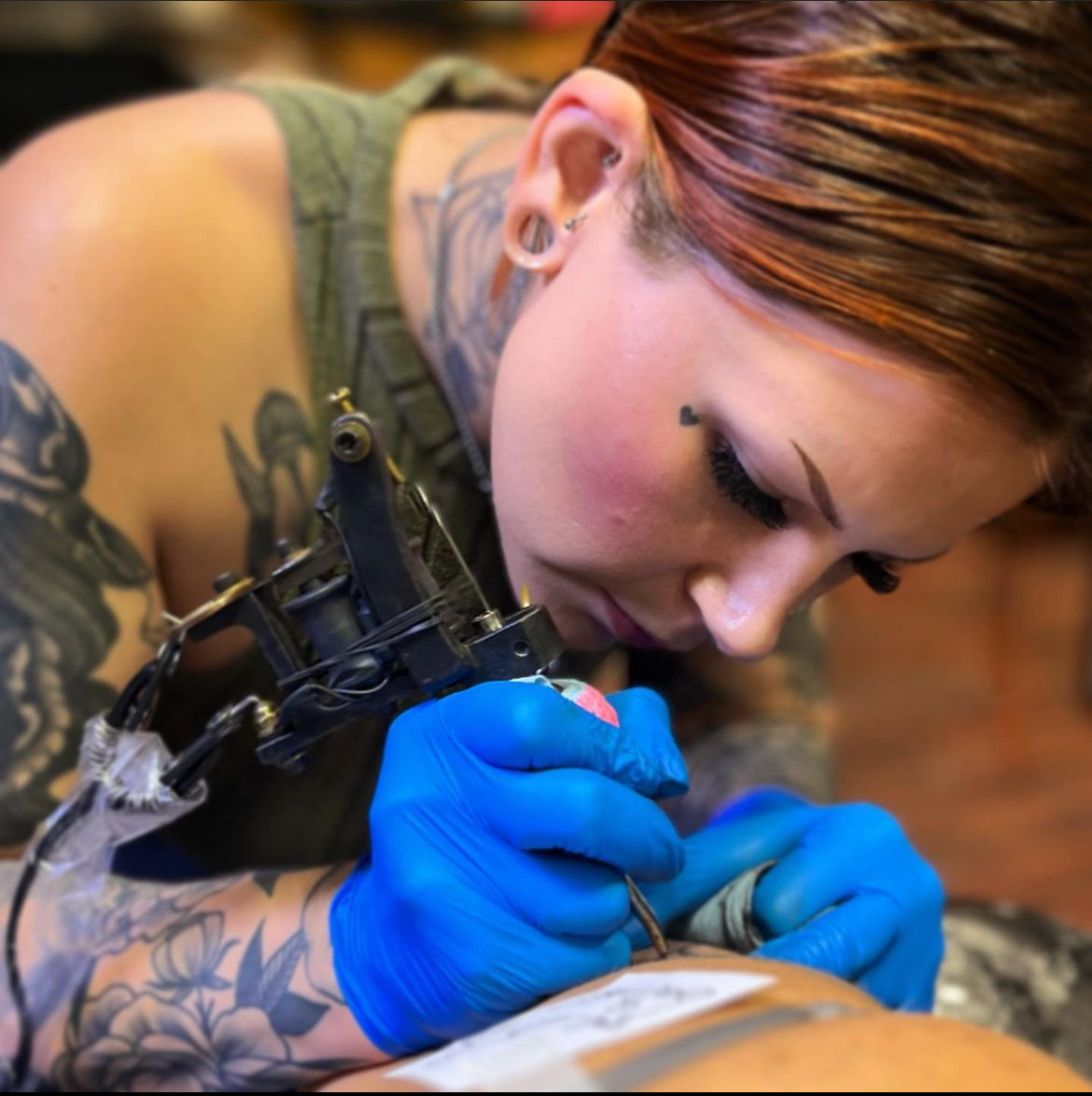 Tattoo artist in blue gloves working with a tattoo machine on a client's arm close-up