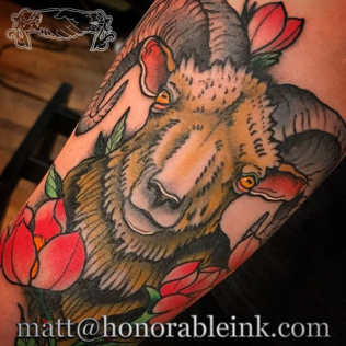 Goat tattoo with red flowers on skin, in black, gray, and tan ink