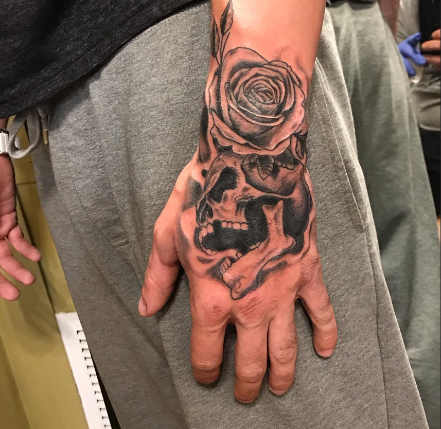 Back of hand with a black skull and rose tattoo on the wrist and hand
