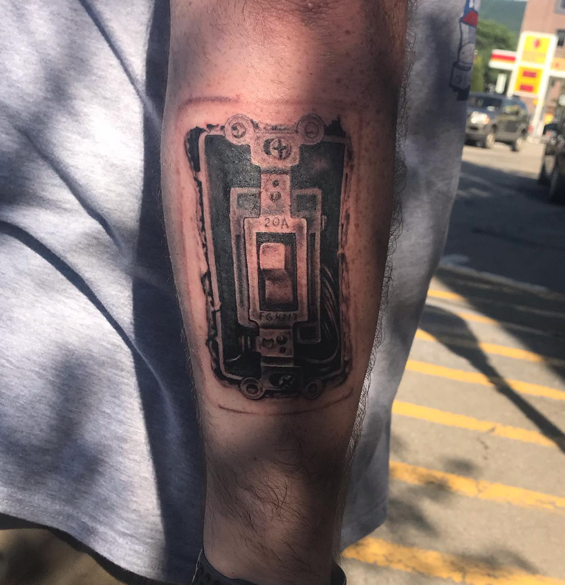 Tattoo on a forearm, showing a dark geometric design with pink accents outdoors