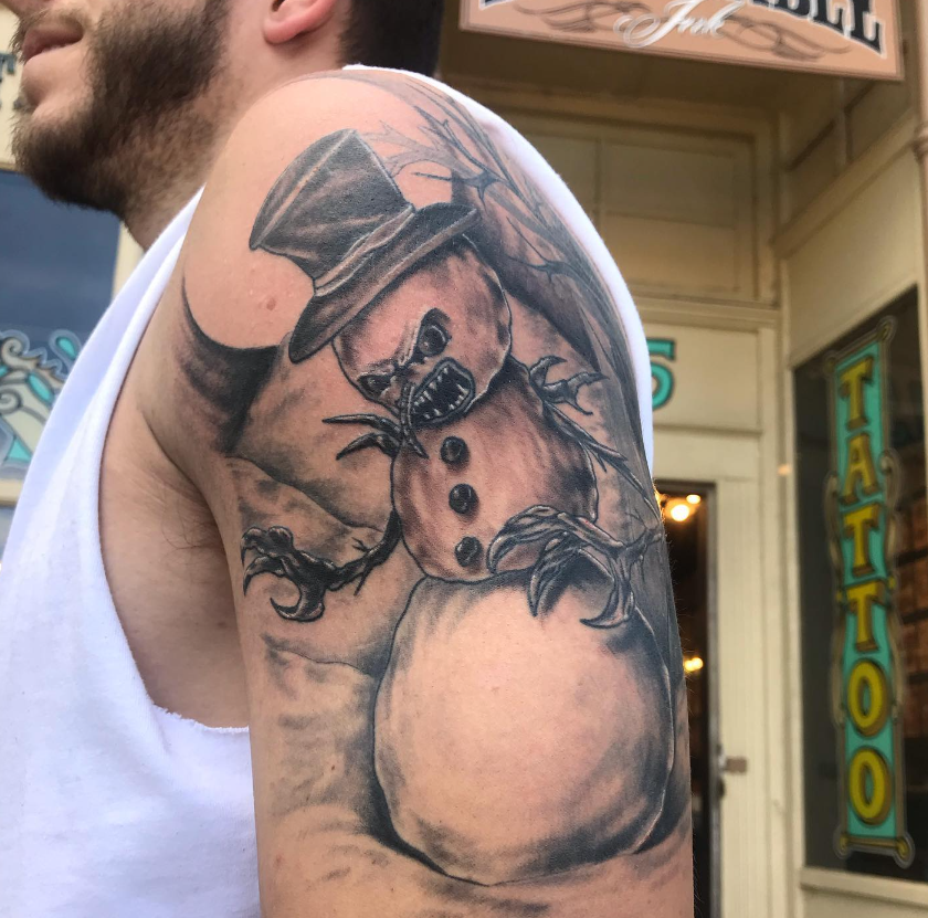 Arm tattoo of a cowboy in a hat, drawn in black and gray, on a person's upper arm.