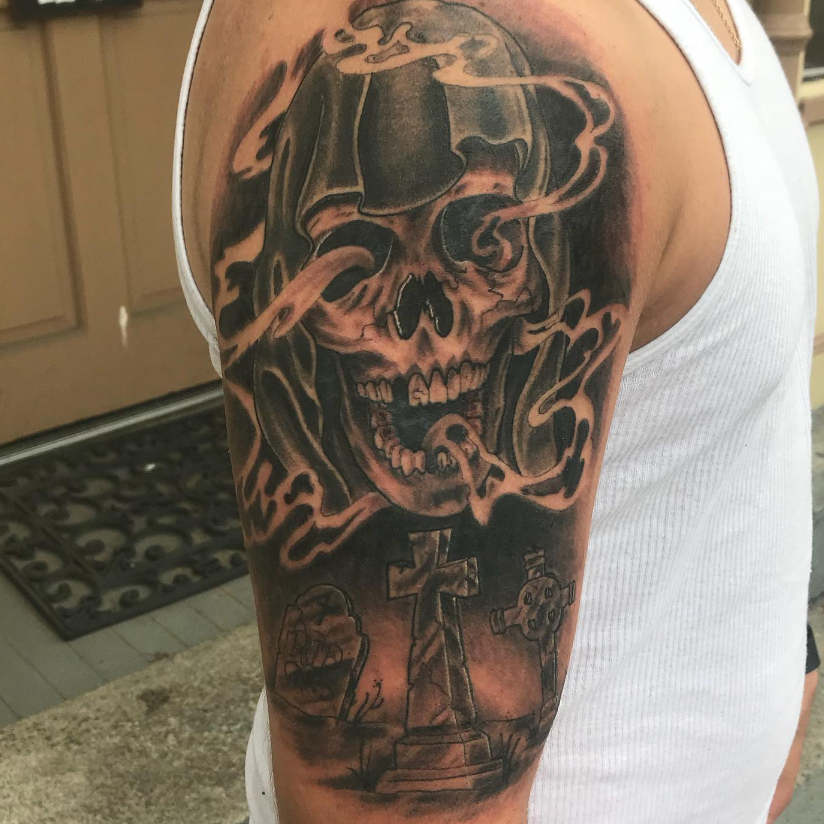 Arm tattoo of a skull with smoke and a cross in black and gray ink