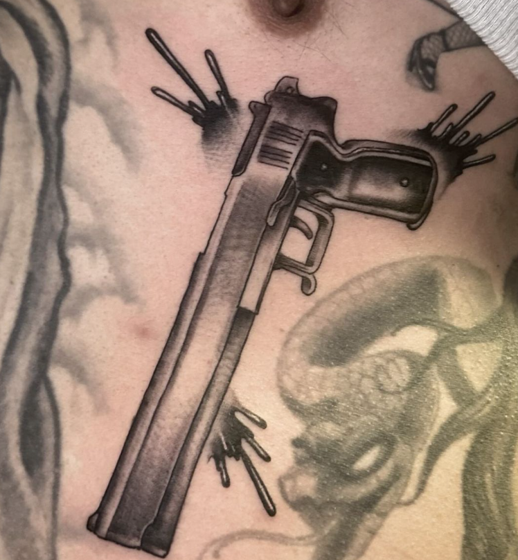 Black-and-gray tattoo of a handgun with small arrow details on skin