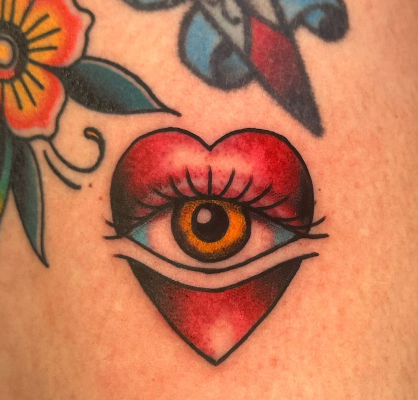 Heart-shaped eye tattoo with red eyelids and an orange iris on skin