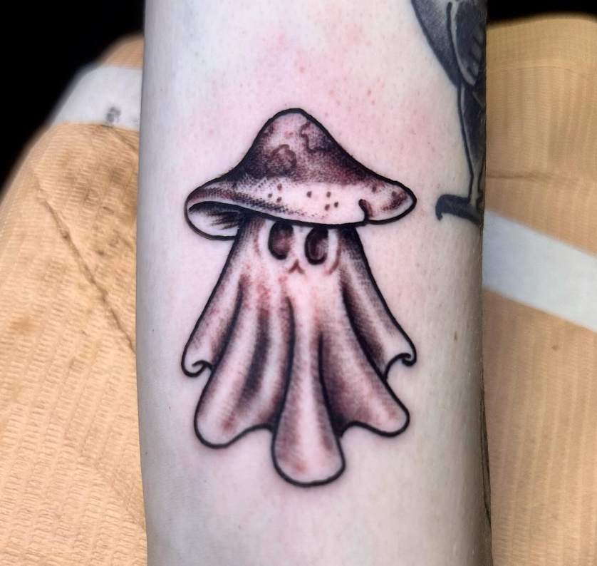 Small pink and black ghost mushroom tattoo on a forearm
