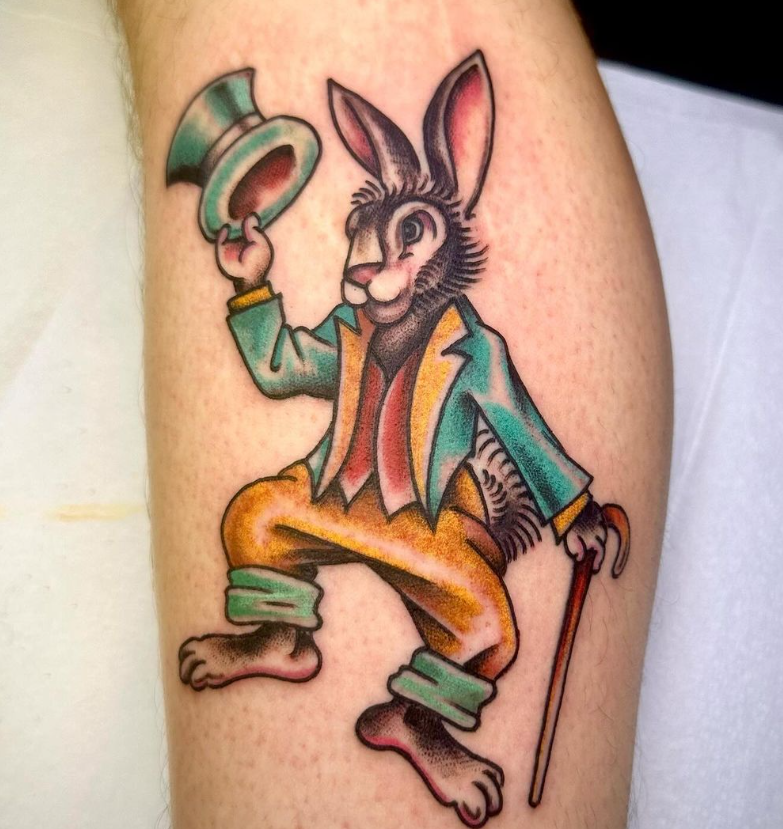 Colorful tattoo of a dapper rabbit in a teal jacket, orange pants, and top hat, holding a cane.