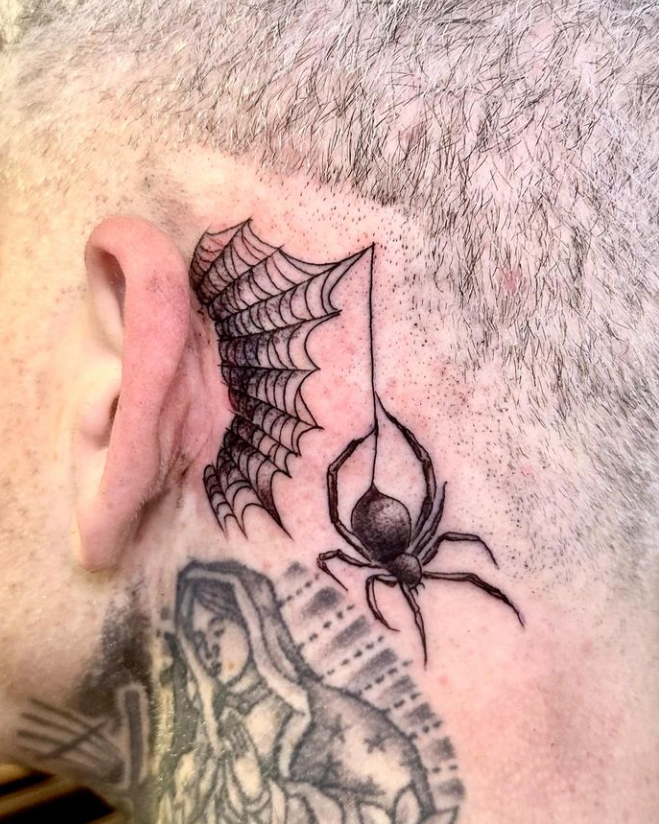 Close-up of a black spiderweb tattoo behind an ear with a hanging spider design.