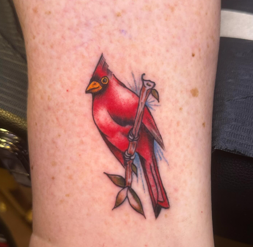 Small red cardinal tattoo perched on a branch on a person’s skin