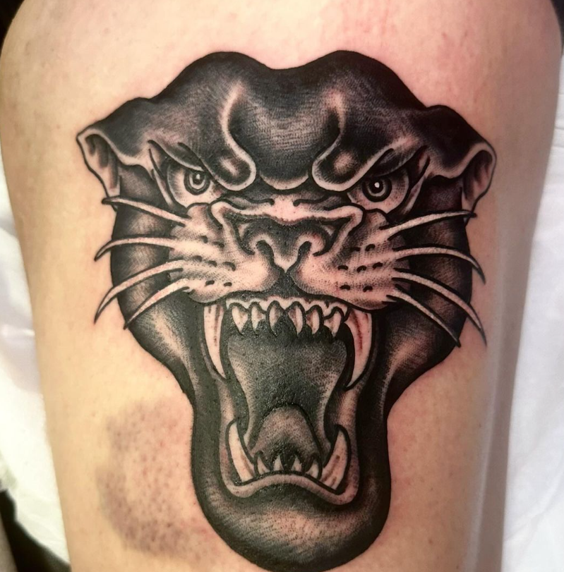 Black panther tattoo with open mouth and bared fangs on a person’s skin