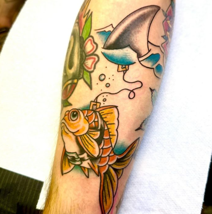 Colorful tattoo sleeve with a fish and flower near a shark fin on a forearm.