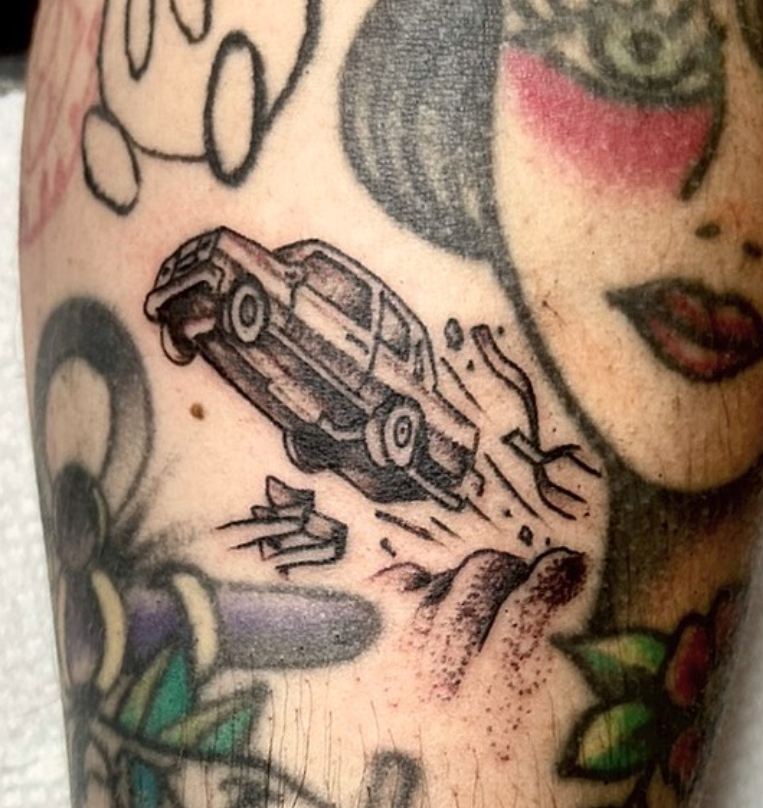 Tattoo of a car crashing through a wall beside a woman’s face with red eye makeup