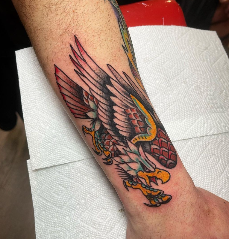 Tattooed forearm with a colorful bird and snake design being worked on, resting on a white towel.