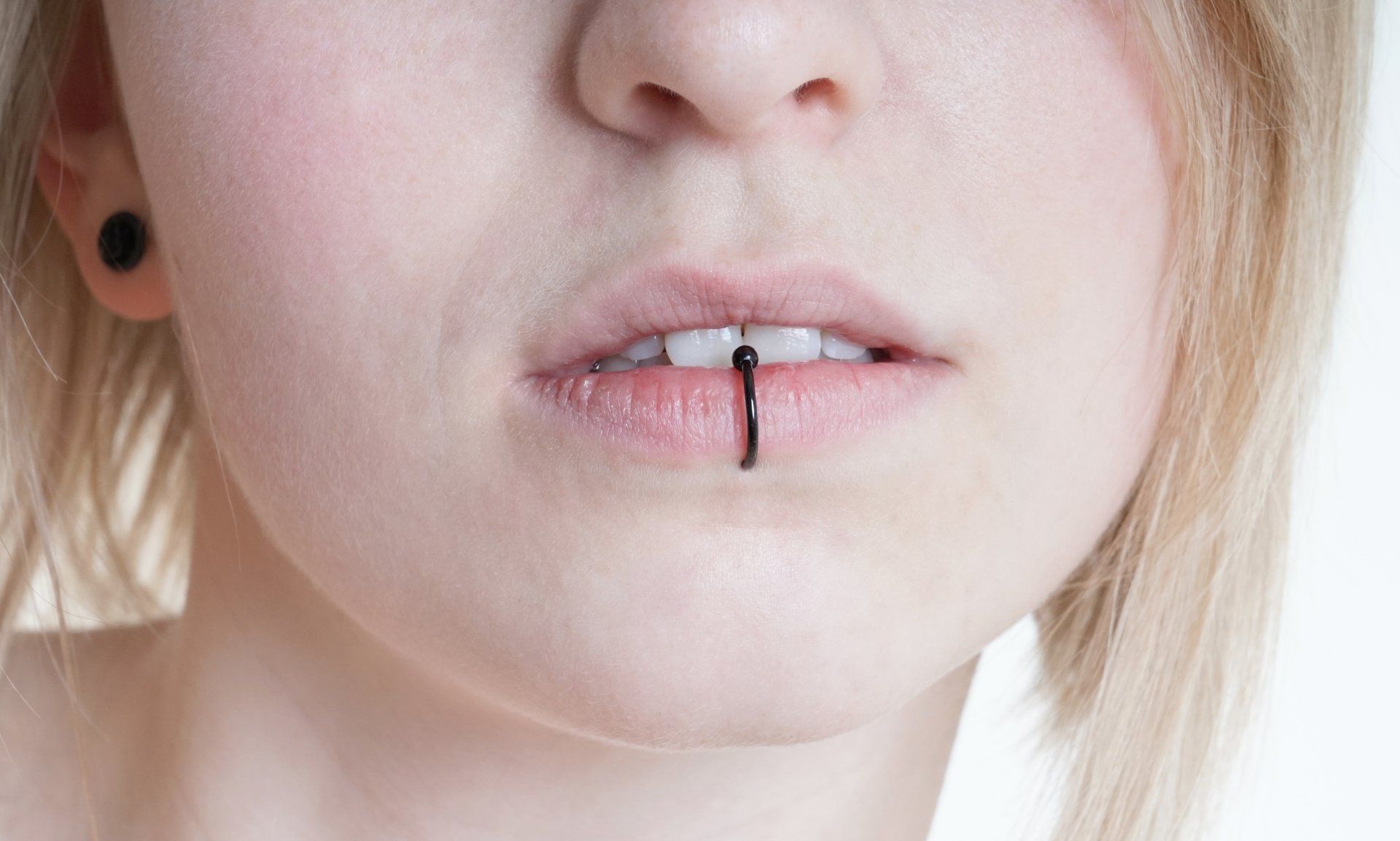 Close-up of lips with a black vertical lip piercing against pale skin