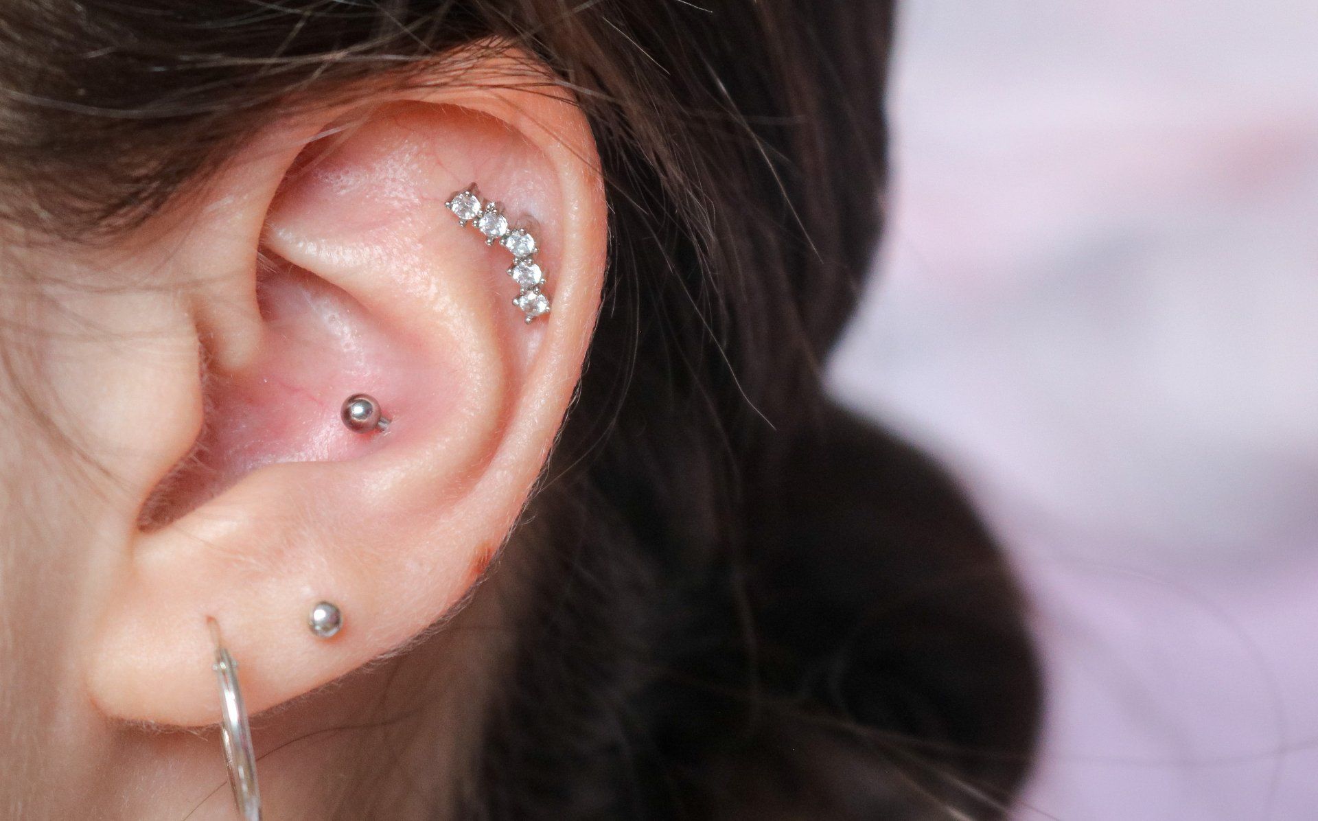 Close-up of an ear with multiple silver piercings and a small dangling earring