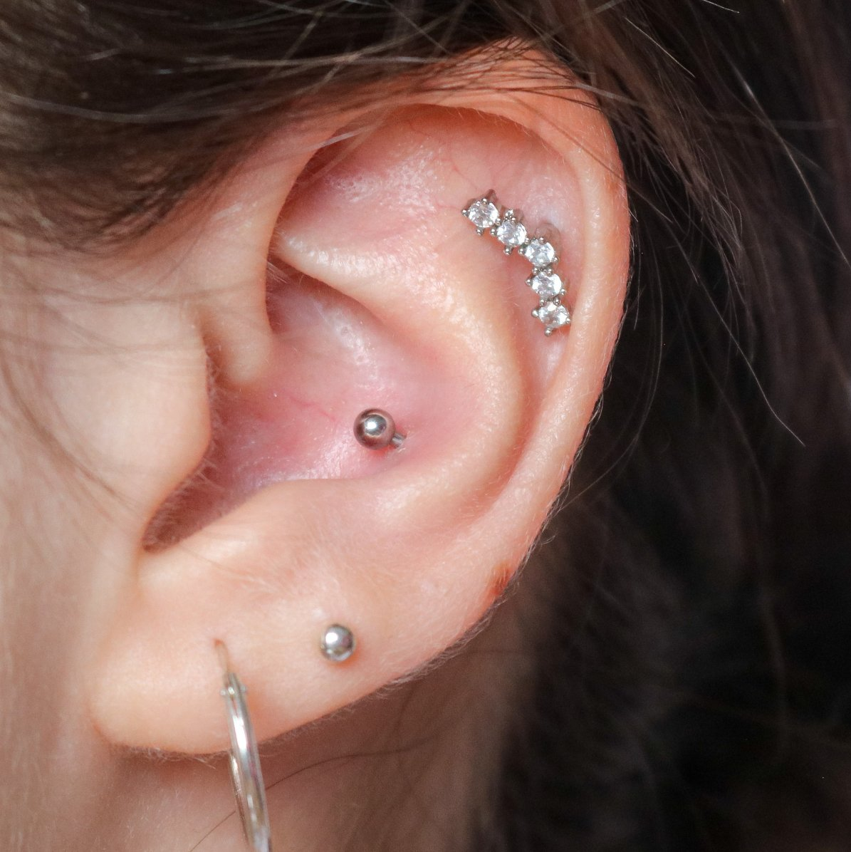Close-up of an ear with multiple piercings and silver jewelry, including a curved stud and hoop.