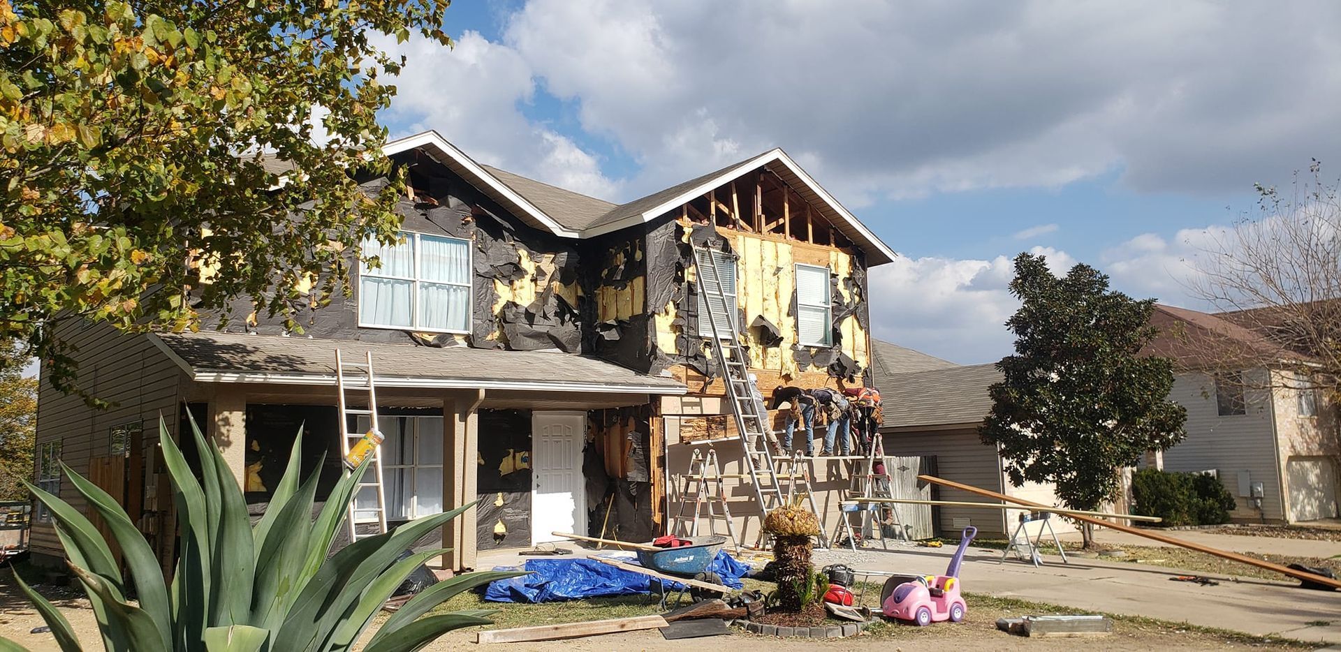 A two-story house with significant fire damage to its exterior siding and upper level, situated in a residential area.