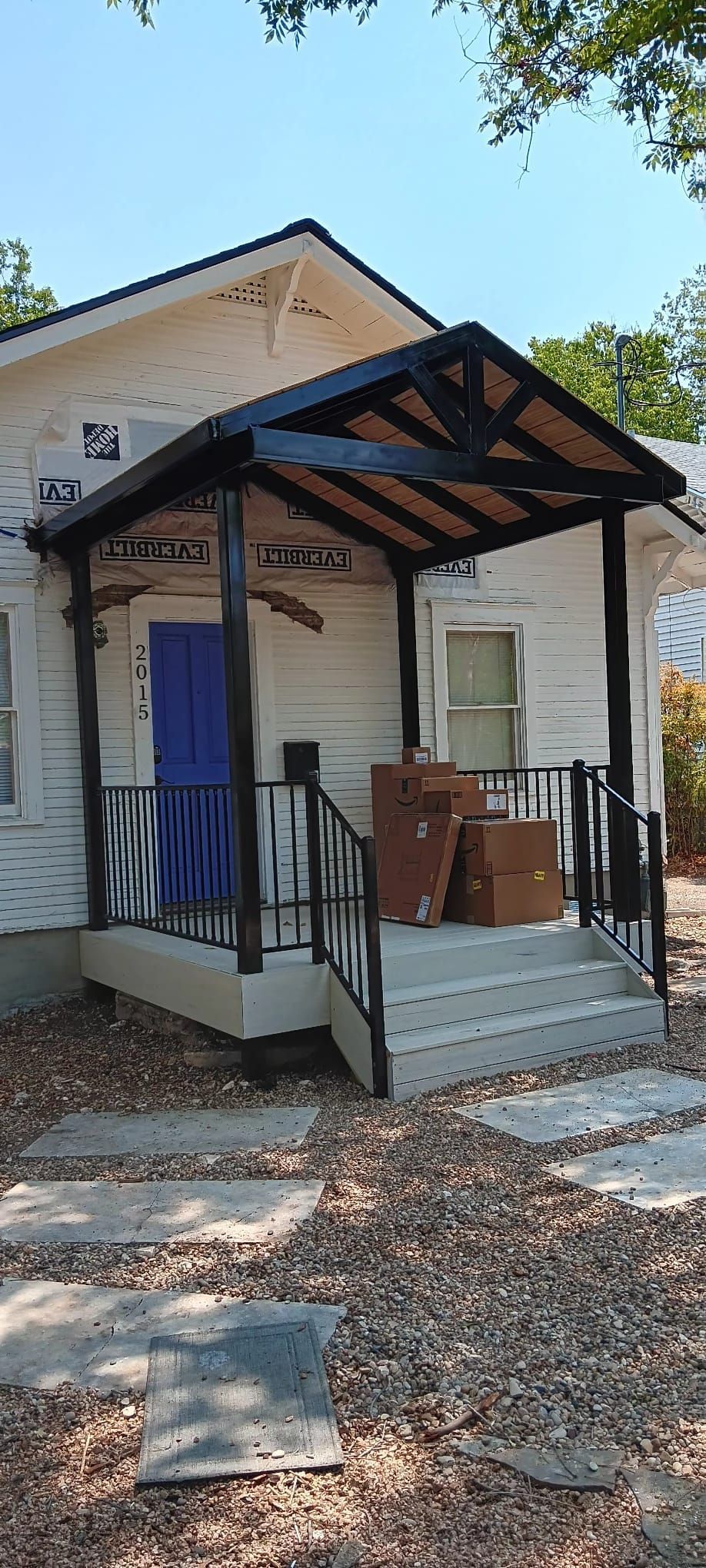 A white cottage with a black porch, a bright blue door, and boxes stacked on the concrete stairs.