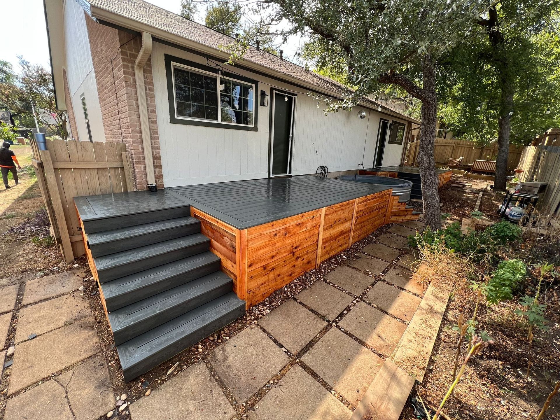 A modern gray deck with matching stairs and cedar wood skirting attached to the rear of a white house with stone trim.
