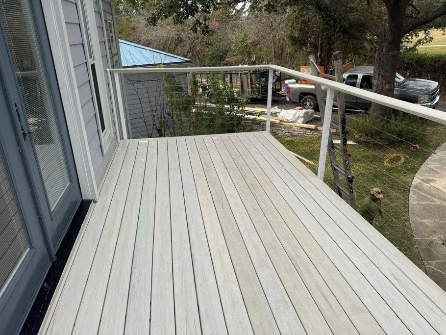 A gray wooden deck with white railing, viewed from a doorway, overlooking a yard with a parked truck and a blue shed. A gray wooden deck with white railing, viewed from a doorway, overlooking a yard with a parked truck and a blue shed.